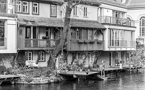 Detailreiche Schwarz-Weiß-Fotografie einer Häuserzeile direkt am Wasser in der Erfurter Altstadt, mit Balkonen, Bäumen und verwinkelter Bebauung – aufgenommen von Fotograf Michael Schalansky.